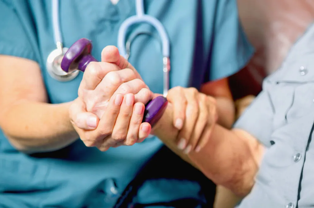 Verpleegster neemt hand van oude patiënt