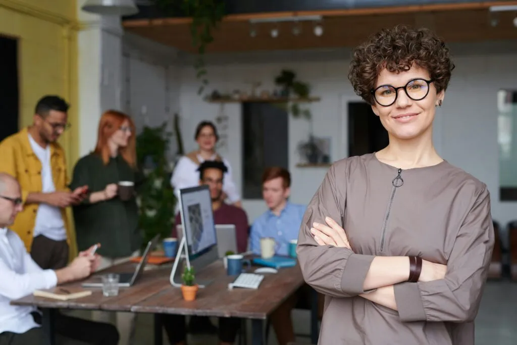 Femme à lunettes souriant avec un groupe de personnes derrière elle Femme à lunettes souriant avec un groupe de personnes derrière elle